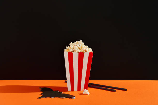 istock Striped box with popcorn, bat napkin and straws on an orange black background 1718500660