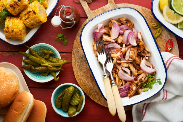 istock Pulled bbq chicken with baked onions on serving platter, bbq corn, pickles, chili peppers and buns for hot dogs and burgers, tomato sauce. Traditional American grilled summer bbq sandwiches dishes. 1718504607