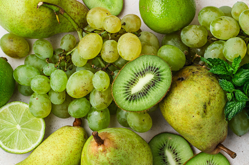 Top view of green colour fruits. Bunch of grapes, kiwis, pears, lime and mint on white background.