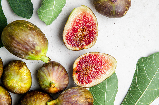 Top view of organic figs and cut figs on white background with leaves. Top view of a fresh whole and cut figs.