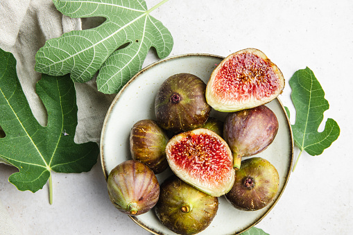 Plate of figs and cut figs on white background with leaves. Top view of a fresh whole and cut figs in plate.