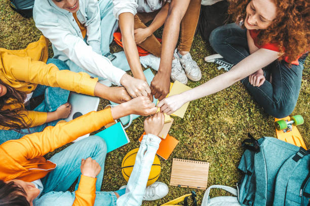 Multicultural university students stacking hands together in college campus - Young people hugging outside symbolizing unity and teamwork
