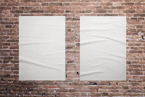 Two blank, white A3 posters are glued to the brick wall. Ideal surfaces for mockup graphic design promotion