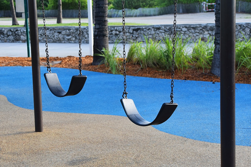 An empty children's swing sways gently in a vibrant Miami Beach playground, its bright colors contrasting with the azure sky and golden sands.