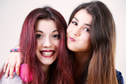 Portrait of two playful young women, possibly sisters or friends, making funny faces. With well-done makeup and long hair, they embrace the silliness of youth and beauty