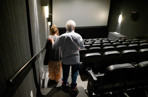 Rear view of senior couple entering cinema hall going to their seat during movie show time