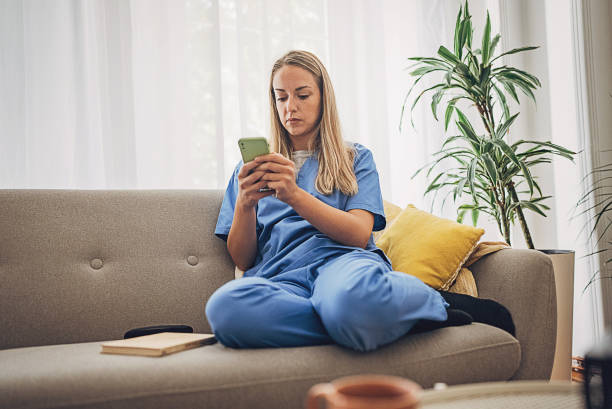 istock Female nurse came back from work and still wearing scrubs relaxing at home and using mobile phone 1718569455