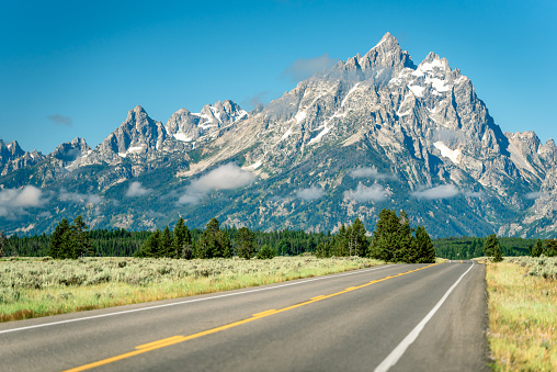 The Teton Park Road disappears into the distance as the snow-capped peaks of the Grand Teton mountains tower above in Grand Teton National Park, Wyoming.
