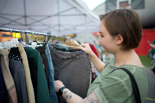 Young woman choosing second hand clothes at a flea market. Zero waste and sustainable lifestyle concept.