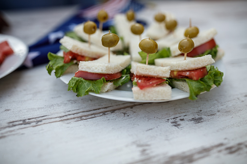 Close up shot of a plate of delicious finger sandwiches with olives on top served on a table for a 4th of July party on the balcony.