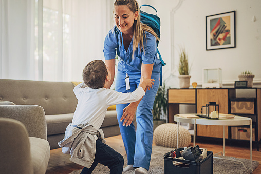 Female nurse wearing scrubs playing with her son at home after work