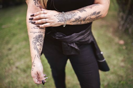 Mid section of a fashionable tattooed woman wearing black nail paint while standing outside