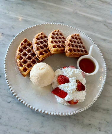 Close up shot of a plate with sweet waffles and coffee served on a tray as a breakfast in bed. There is also a single macaroon and a tulip for decoration.