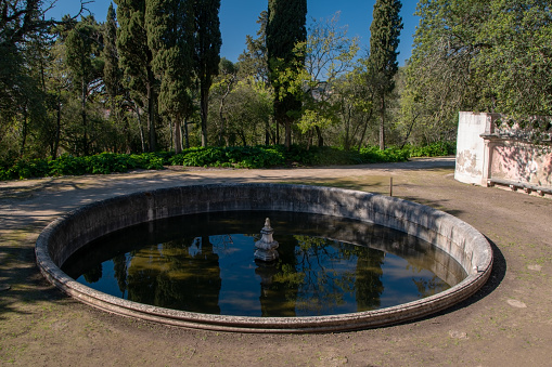 A serene green park in Lisbon, Portugal, features a historical fountain and monument within Lisbon Garden, offering a tranquil and picturesque setting for visitors to enjoy.