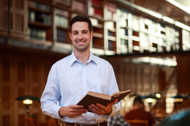 istock Young man reading a book in public library 1718661968