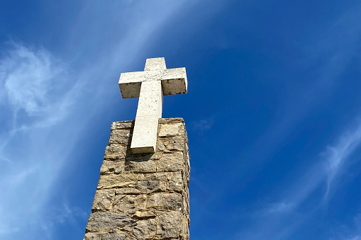 A striking large stone cross stands tall against the vivid blue sky at Cape Da Roca, Cabo da Roca, Portugal, creating a serene and majestic scene.