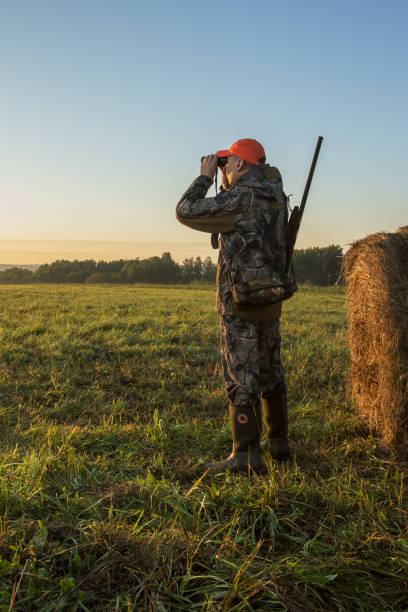 istock Male with a gun looking in binoculars. Hunter man. 1718674404