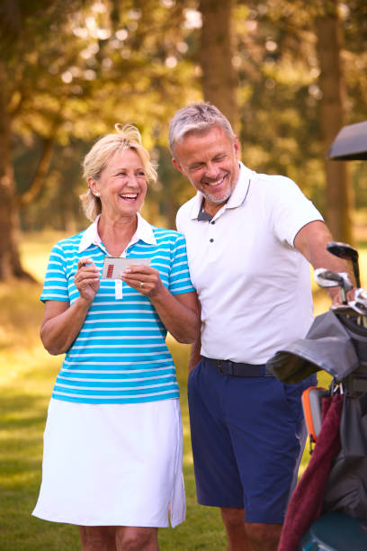 Senior Couple Standing Next To Buggy On Golf Course Marking Score Card Together