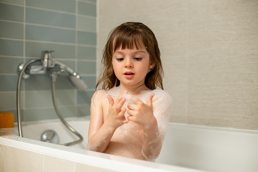 Cute little girl playing with bath foam while taking a bath