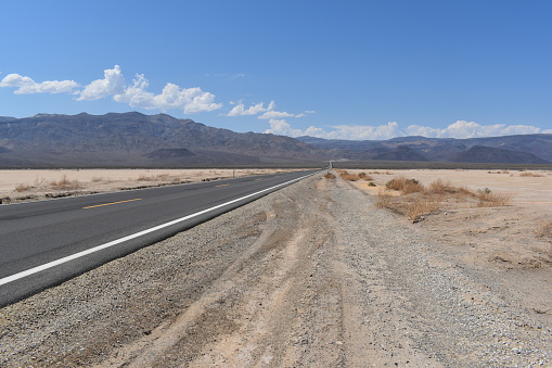 An empty road stretches through the scorching Valley of Death in the hot desert, framed by majestic mountains in a US national park.
