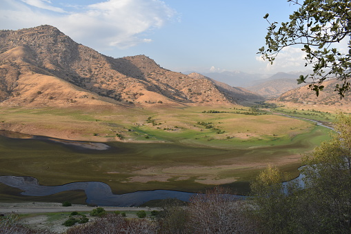 A breathtaking view of a US national park in California, featuring majestic mountains and a serene river meandering through a picturesque valley. The landscape is adorned with California hills, creating a beautiful natural scene at sunset. Wildlife thrives in this pristine environment, making it a perfect blend of hills and plains.