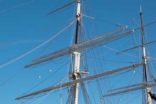 Vintage old sailing ship mast with clear blue sky background. Sail and mast with rigging and guys of an old sailing ship