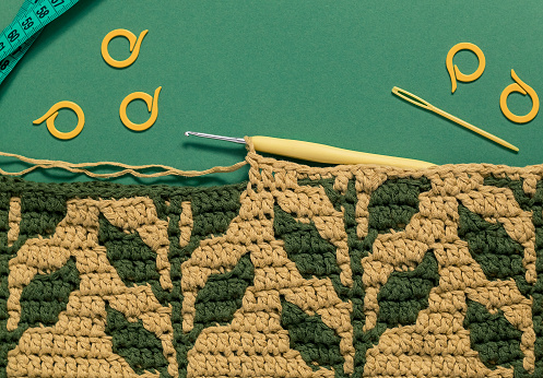 Crocheting warm blanket with yellow green foliage pattern. Crochet work in process. Top view. Copy space.