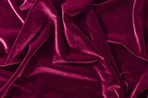 A background of crumpled pinkish red / maroon velvet with a luxurious sheen.