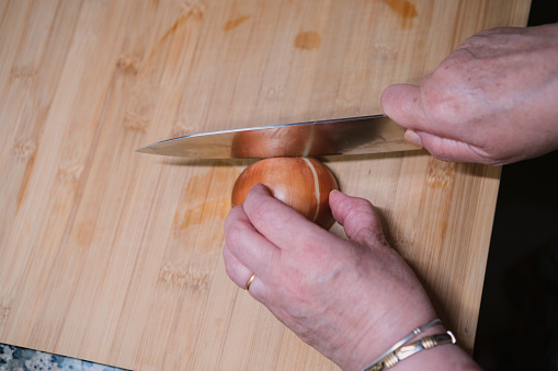 Closeup of hands chopping fresh onion on kitchen board.