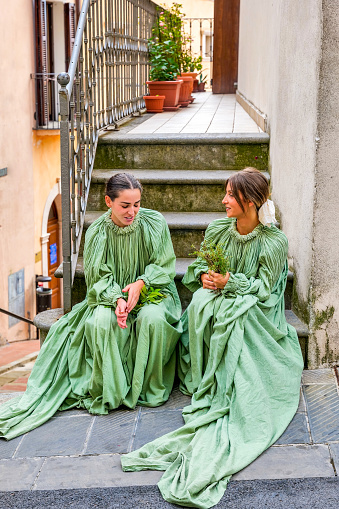 Gualdo Tadino, Umbria, Italy, September 22 -- Two girls in medieval dresses take a break during a historical reenactment in the town of Gualdo Tadino in Umbria, central Italy. The Umbria region, considered the green lung of Italy for its wooded mountains, is characterized by a perfect integration between nature and the presence of man, in a context of environmental sustainability and healthy life. In addition to its immense artistic and historical and medieval heritage, Umbria is famous for its food and wine production and for the high quality of the olive oil produced in these lands. Image in high definition quality.