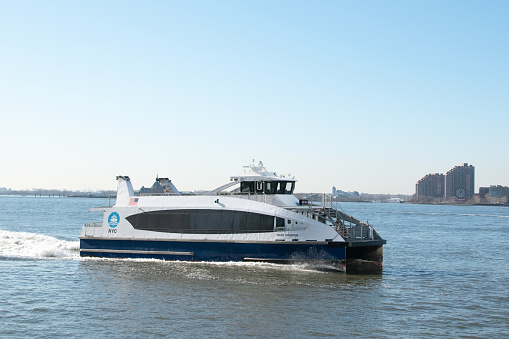 A New York City ferry docked in the Financial District of Manhattan, surrounded by iconic skyscrapers and the hustle and bustle of downtown NYC.