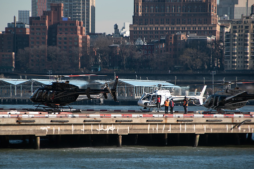A taxi helicopter sits poised for takeoff at a bustling terminal in New York City's financial district, offering premium helicopter charter services amid the iconic Manhattan skyline.