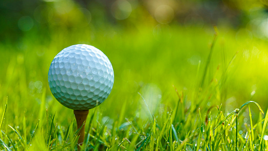 One broken white golf ball lays on green grass. Damaged golf ball