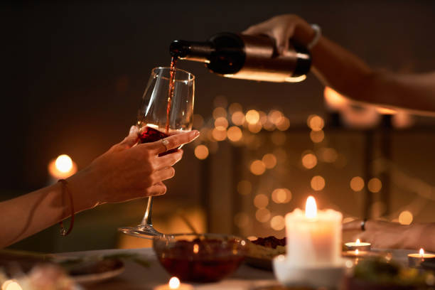 Two people pouring red wine into glass enjoying dinner with candles Side view closeup of two people pouring red wine into glass while enjoying dinner with candles, copy space gay dinner table stock pictures, royalty-free photos & images
