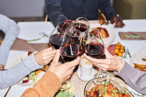 夕食の席で赤ワイングラスで乾杯する友人のグループの接写 - dining table flash ストックフォトと画像