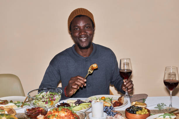 夕食の席で自家製の食べ物を楽しむ笑顔の若いアフリカ系アメリカ人男性 - dining table flash ストックフォトと画像