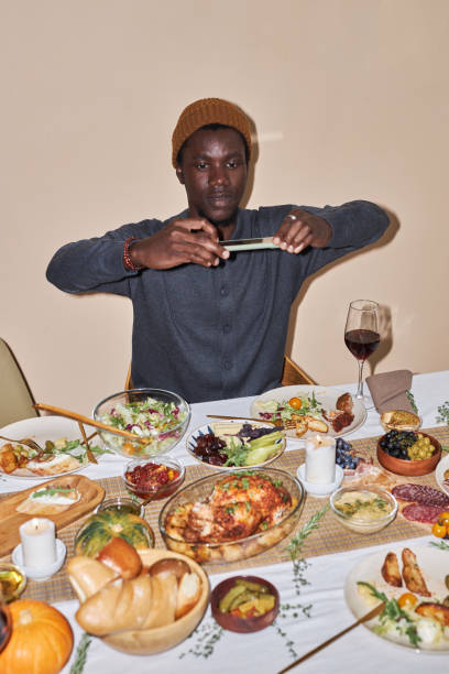 молодой чернокожий мужчина фотографирует обеденный стол в день благодарения, снятый со вспышкой - dining table flash стоковые фото и изображения