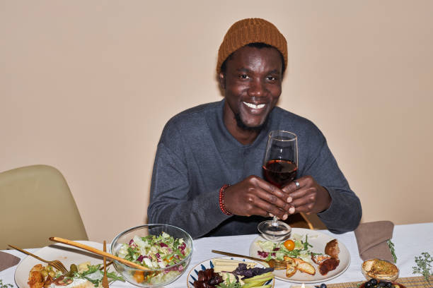 черн�ый мужчина улыбается в камеру и держит бокал вина за обеденным столом - dining table flash стоковые фото и изображения