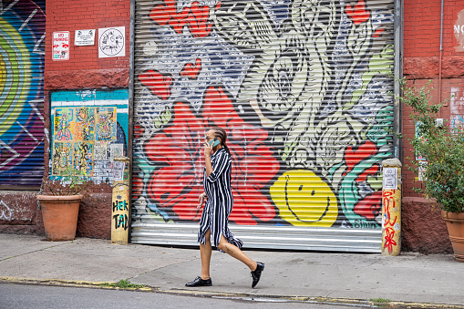West 27th Street, Manhattan, New York, USA - August 17th 2023: One young woman with a smart phone passing a colorful door to a professional garage