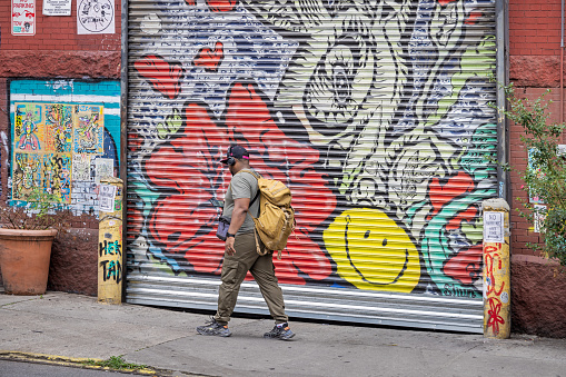 West 27th Street, Manhattan, New York, USA - August 17th 2023: Man with a backpack passing a colorful door to a professional garage