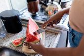 Close-up of a woman cutting a watermelon on kitchen counter at home