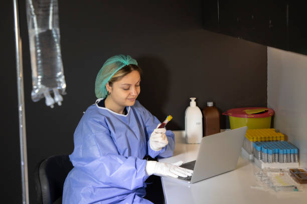 a young blonde medical staff member is holding a blood tube and typing information on her laptop in the clinic. - dentist office nurse doctors office blond hair imagens e fotografias de stock