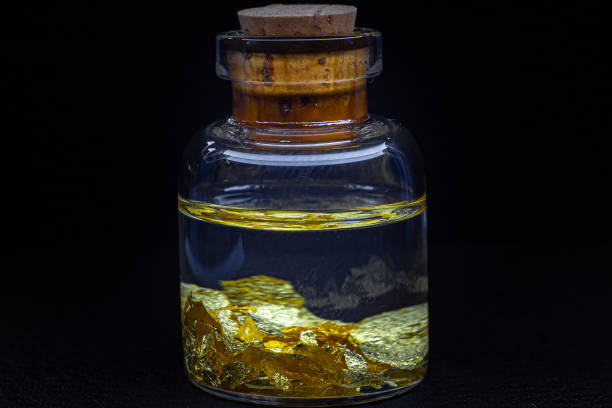 una bottiglietta di vetro con un tappo di legno su una superficie nera con macro foglie d'oro 22 carati - gold leaf gold flakes gilded foto e immagini stock