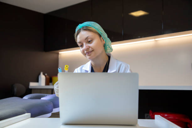 a young blonde medical staff member is holding a blood tube and typing information on her laptop in the clinic. - dentist office nurse doctors office blond hair imagens e fotografias de stock