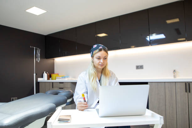 a young blonde medical staff member is holding a blood tube and typing information on her laptop in the clinic. - dentist office nurse doctors office blond hair imagens e fotografias de stock