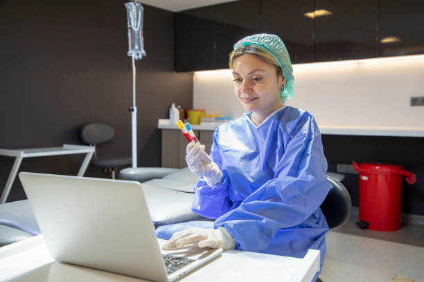 a young blonde medical staff member is holding a blood tube and typing information on her laptop in the clinic. - dentist office nurse doctors office blond hair imagens e fotografias de stock
