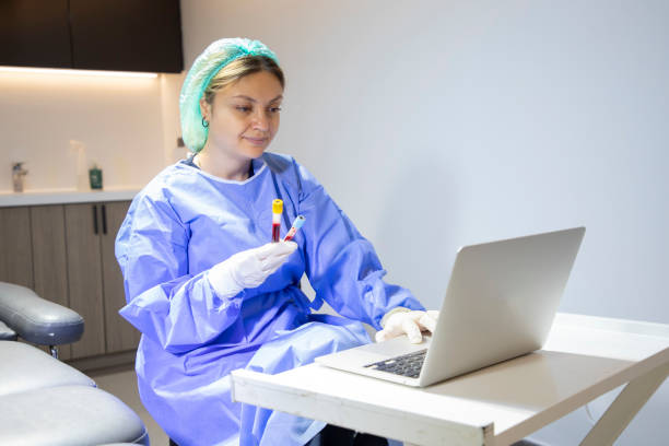 a young blonde medical staff member is holding a blood tube and typing information on her laptop in the clinic. - dentist office nurse doctors office blond hair imagens e fotografias de stock