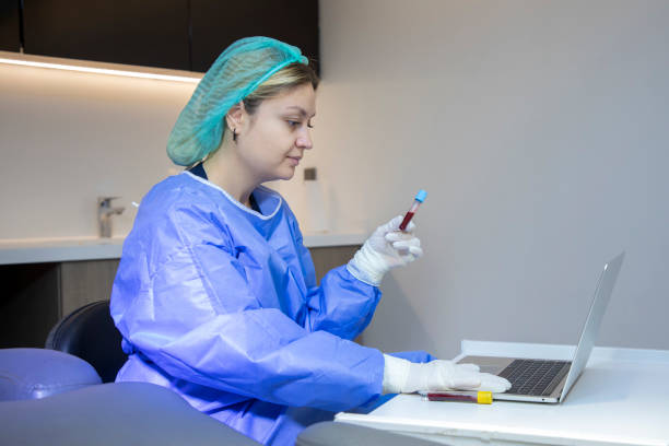 a young blonde medical staff member is holding a blood tube and typing information on her laptop in the clinic. - dentist office nurse doctors office blond hair imagens e fotografias de stock