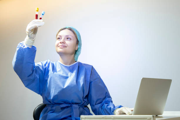 a young blonde medical staff member is holding a blood tube and typing information on her laptop in the clinic. - dentist office nurse doctors office blond hair imagens e fotografias de stock