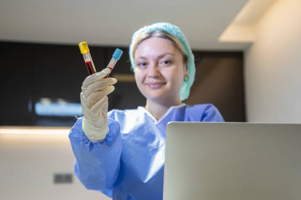 a young blonde medical staff member is holding a blood tube and typing information on her laptop in the clinic. - dentist office nurse doctors office blond hair imagens e fotografias de stock